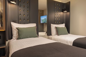 A hotel room with two beds, each with a pillow and a headboard with a light fixture.