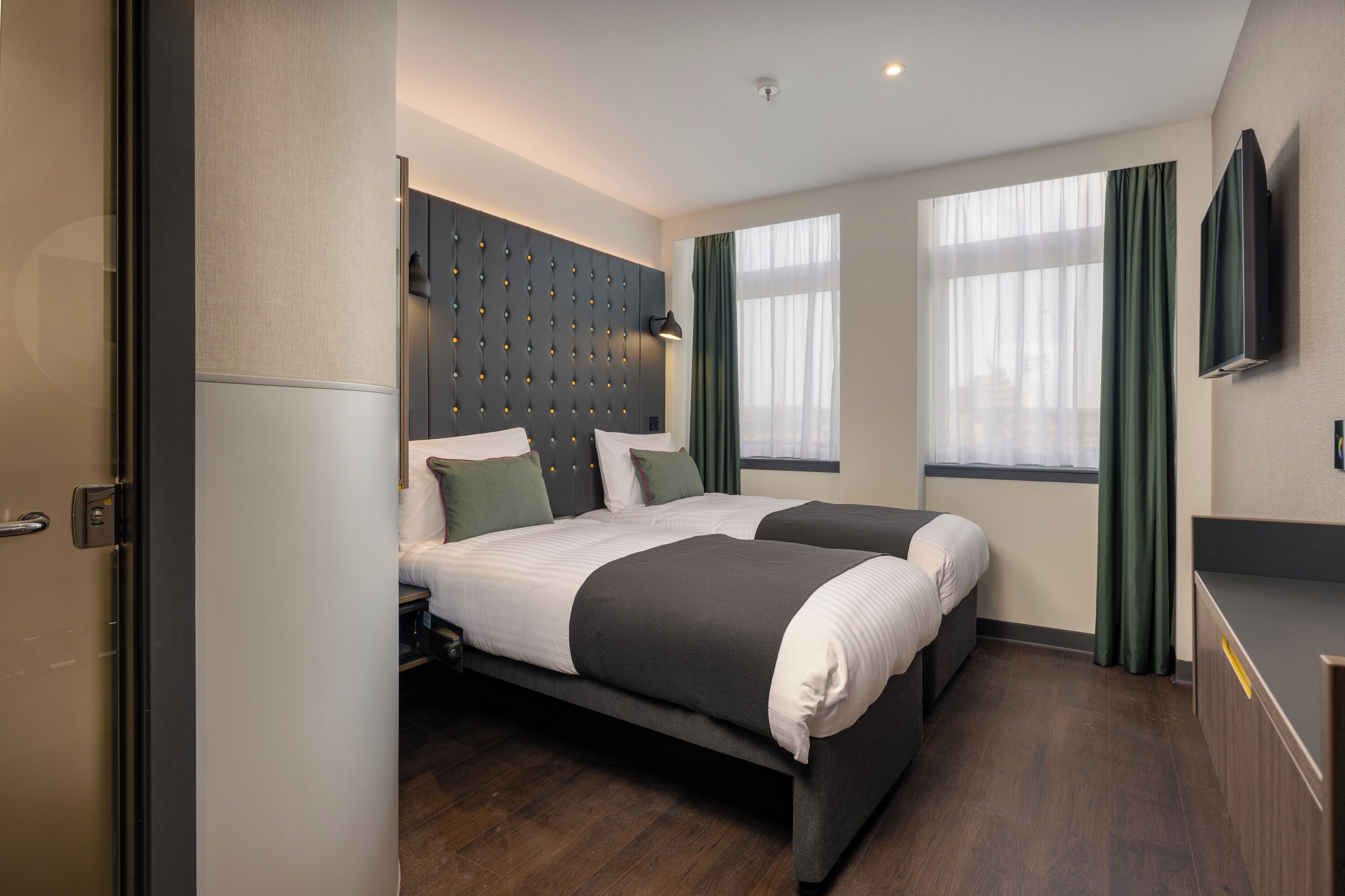 A modern hotel room with a large bed, a flat-screen TV, and a large window with curtains.