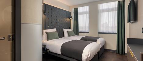 A modern hotel room with a large bed, a flat-screen TV, and a large window with curtains.