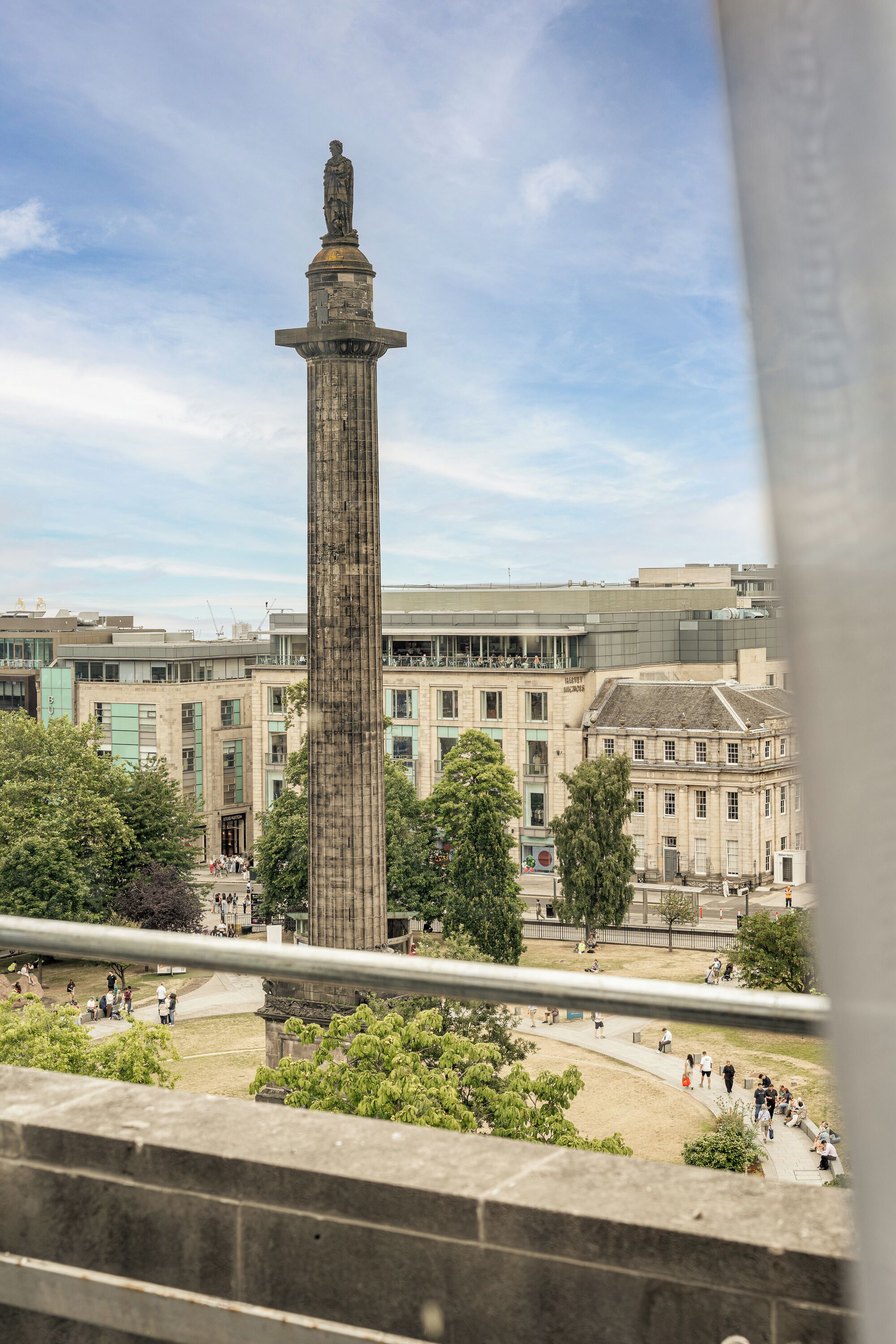 A tall monument in a public square with surrounding buildings and trees.