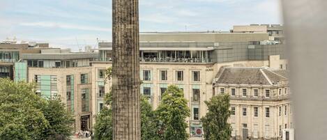 A tall monument in a public square with surrounding buildings and trees.
