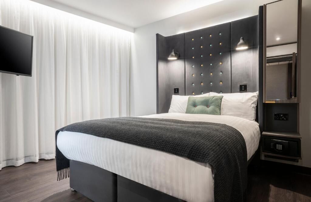 A modern hotel room with a large bed, a flat-screen TV, a wardrobe, and a bedside table.
