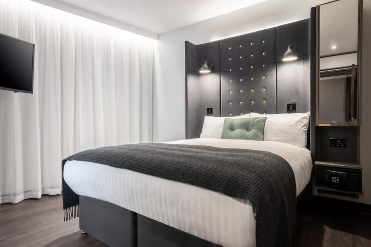 A modern hotel room with a large bed, a flat-screen TV, a wardrobe, and a bedside table.