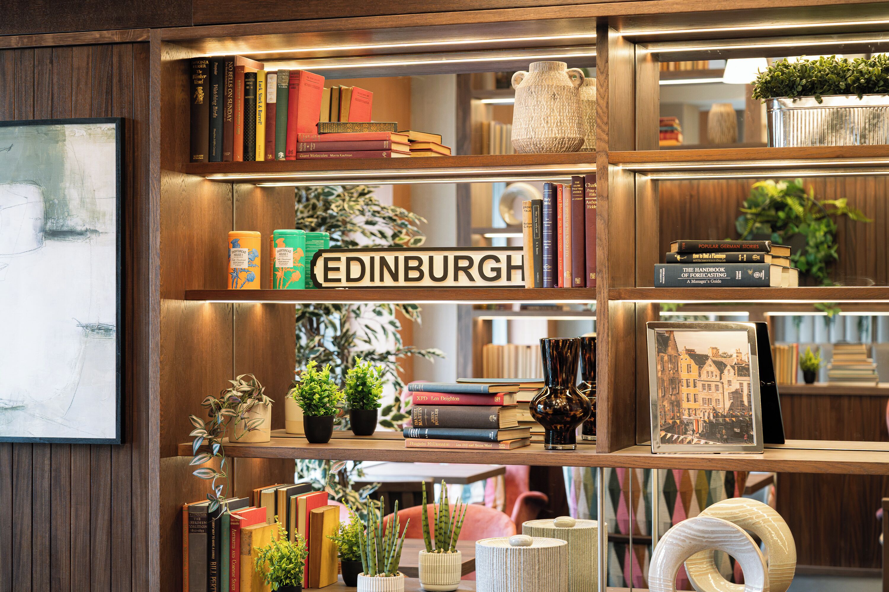 A bookshelf with a variety of books, a sign reading 'EDINBURGH,' and decorative items including plants and vases.