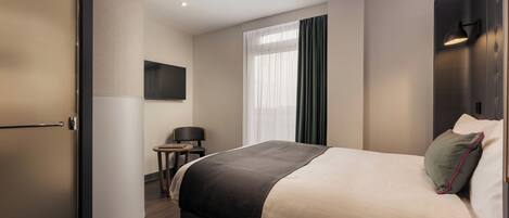 Habitación de hotel con cama, escritorio, silla, televisión y ventana con cortinas.