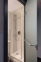 A modern bathroom with a glass shower enclosure, a white sink, and a towel rack.