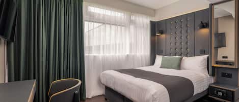 A modern hotel room with a large bed, a desk, and a chair.