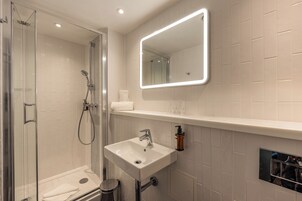 A modern bathroom with a glass-enclosed shower, a white sink, and a mirror above the countertop.