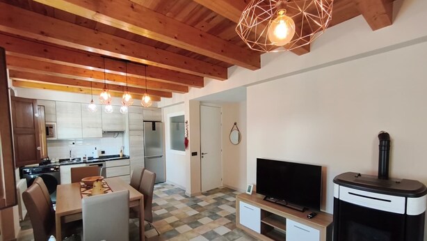Een moderne keuken met houten balken, een eethoek met een zwart-wit geruite vloer, een flatscreen televisie en een houtkachel.