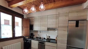 Een keuken met houten kastjes, een roestvrijstalen koelkast, een vaatwasser en een raam met jaloezieën.