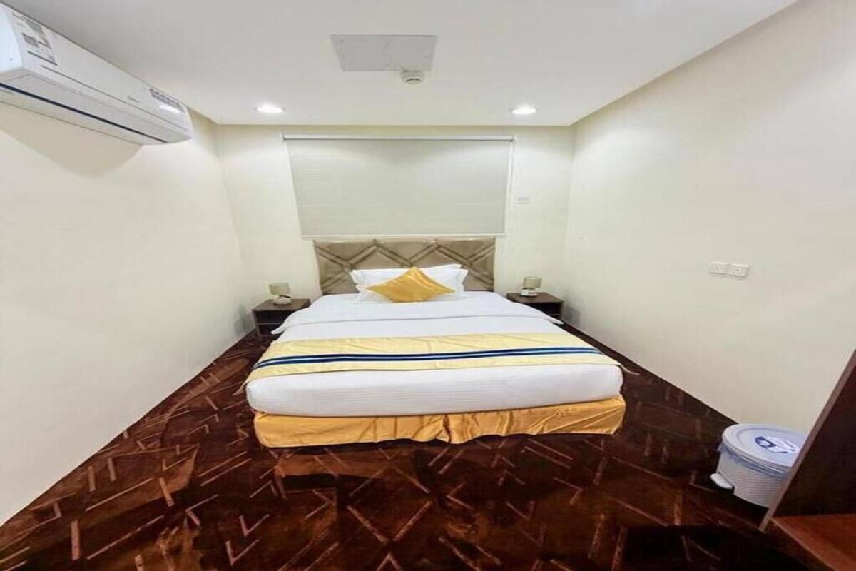 A hotel room with a bed, nightstands, an air conditioning unit, and a trash bin.