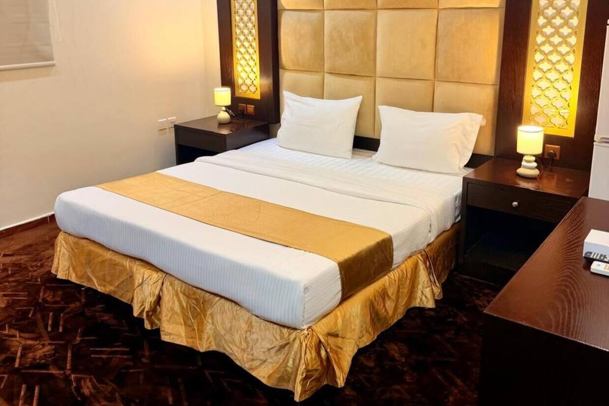 A hotel room with a large bed, a wooden headboard, bedside tables with lamps, and a patterned carpet.
