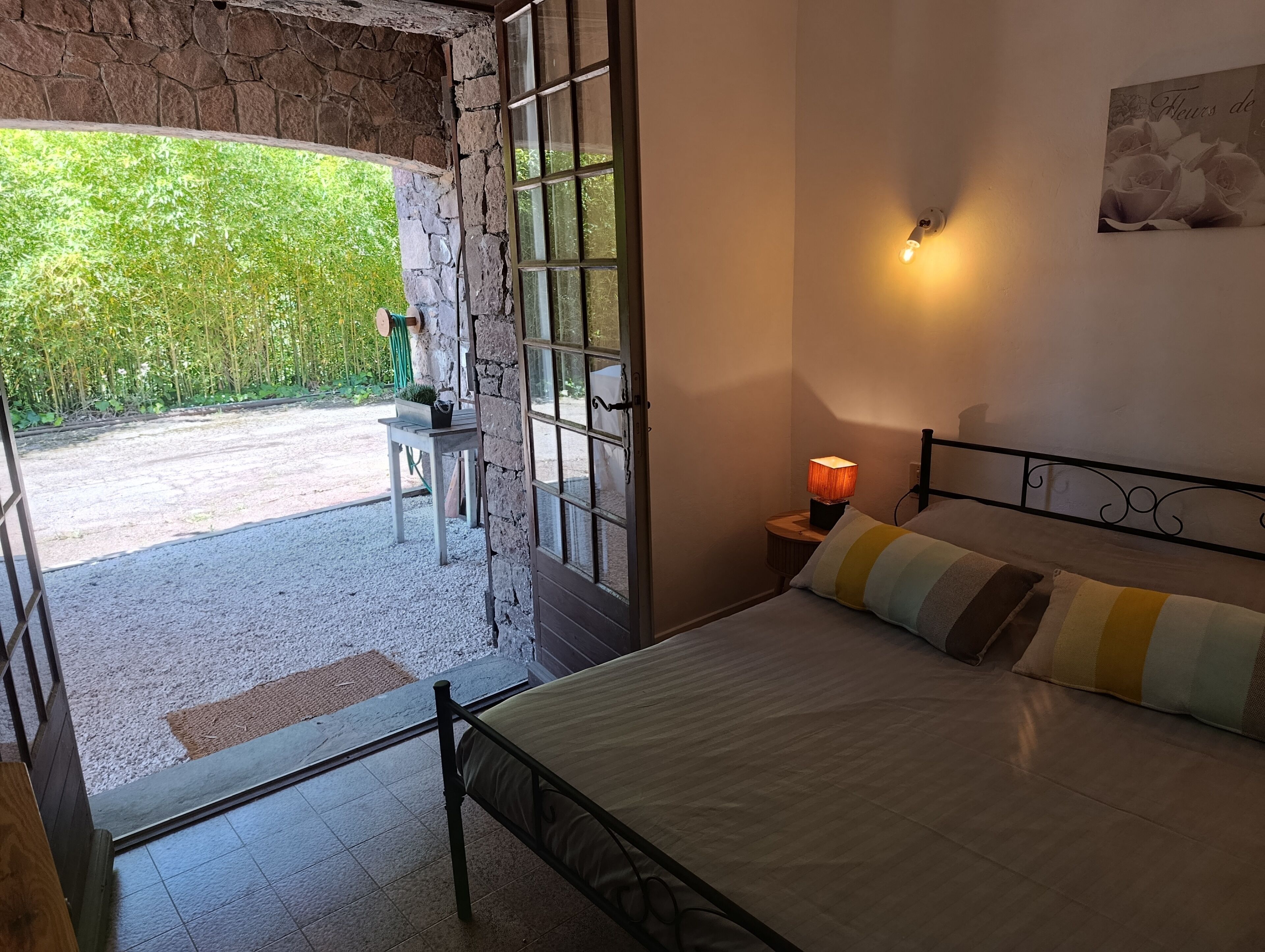 Une chambre à coucher avec un lit, une table de chevet avec une lampe, une chaise et une vue sur la verdure à l’extérieur.