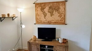 A room with a wooden TV stand, a globe map, a floor lamp, and a shelf with decorative items. - Garden apartment in the countryside near the sea pets welcome (Les Adrets-de-l'Estérel)