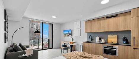 A modern apartment with a large window, a dining area, a kitchenette, and a living space with a sofa and a laptop.