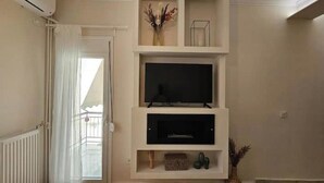 Ein Wohnzimmer mit Fernseher, Kamin und einem Balkon mit weißem Vorhang.