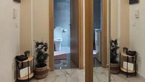 Ein Flur mit einem großen Spiegel, Marmorboden, zwei Zimmerpflanzen und einer Tür zu einem Badezimmer.