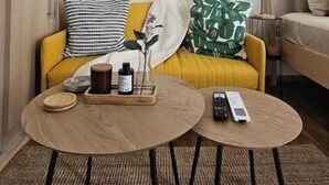 Ein Wohnzimmer mit einem gelben Sofa, zwei runden Couchtischen, einem gewebten Teppich und einem Holzschrank.