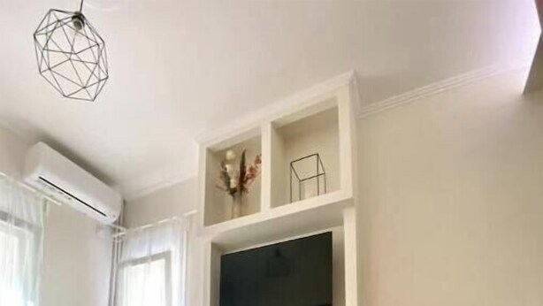 Ein modernes Hotelzimmer mit Flachbildfernseher, einem kleinen Tischchen mit Tablett und einem Bett mit grauer Decke.