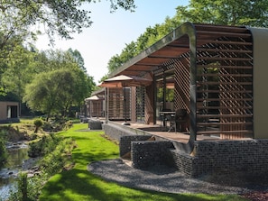 A modern outdoor seating area with tables and chairs, surrounded by a wooden pergola and stone walls.