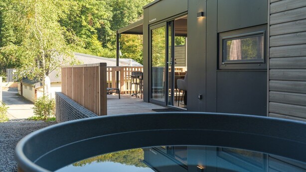 A modern outdoor area with a glass-enclosed hot tub, wooden deck, and a view of a mountain.