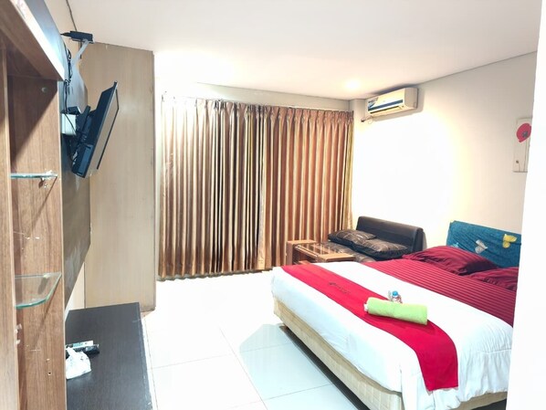 Ein Hotelzimmer mit einem Bett, einem Schreibtisch, einem Sessel, einem an der Wand montierten Fernseher und einem Fenster mit Vorhängen.