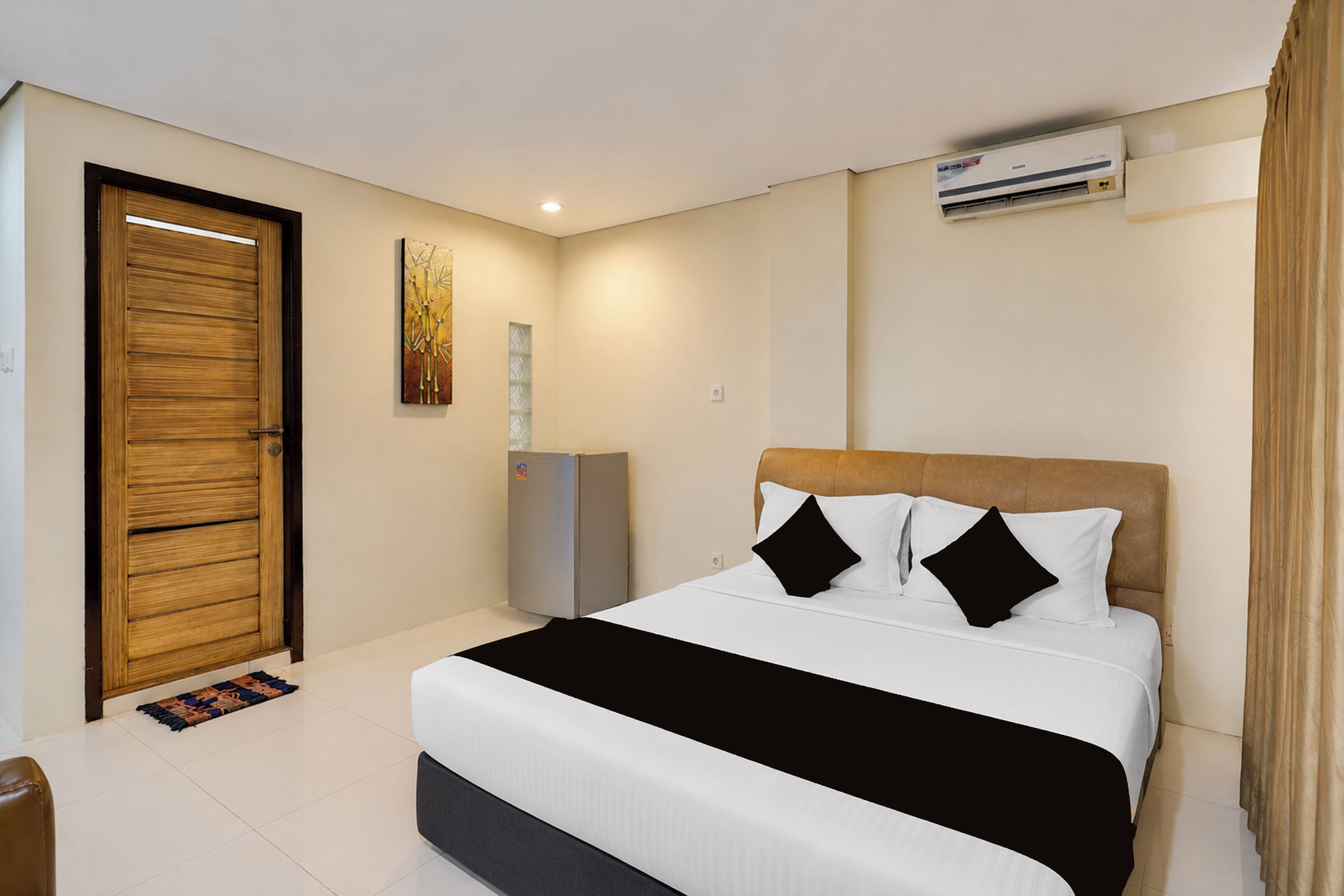 A hotel room with a bed, a wardrobe, a small cabinet, and an air conditioning unit.