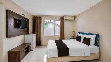 A hotel room with a bed, a TV, a mini-fridge, a window with curtains, and an air conditioning unit.