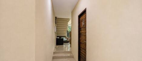 A hallway with a staircase leading to a landing, a door with a number, and a trash bin.