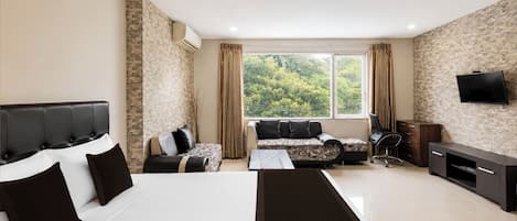 A hotel room with a bed, a sofa, a desk, a TV, and a window with a view of trees.