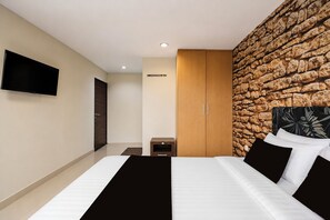 Quarto de hotel moderno com uma cama grande, televisão de tela plana na parede e uma parede de destaque com textura de pedra.