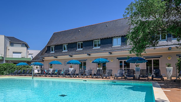 A swimming pool with lounge chairs and umbrellas, a building with a dark roof, and a clear blue sky. - Vannes Apartment With Balcony for 4 (Plescop)