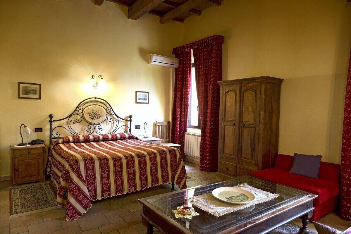Un dormitorio con cama, un armario de madera, un sofá rojo, una mesa de centro de vidrio y un equipo de aire acondicionado.