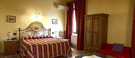 A bedroom with a bed, a wooden cabinet, a red sofa, a glass coffee table, and an air conditioning unit.