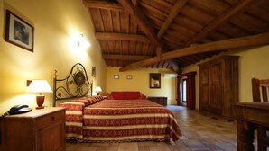 Un dormitorio con techo de madera, una cama con colcha estampada, una mesita de noche con lámpara y un armario de madera.