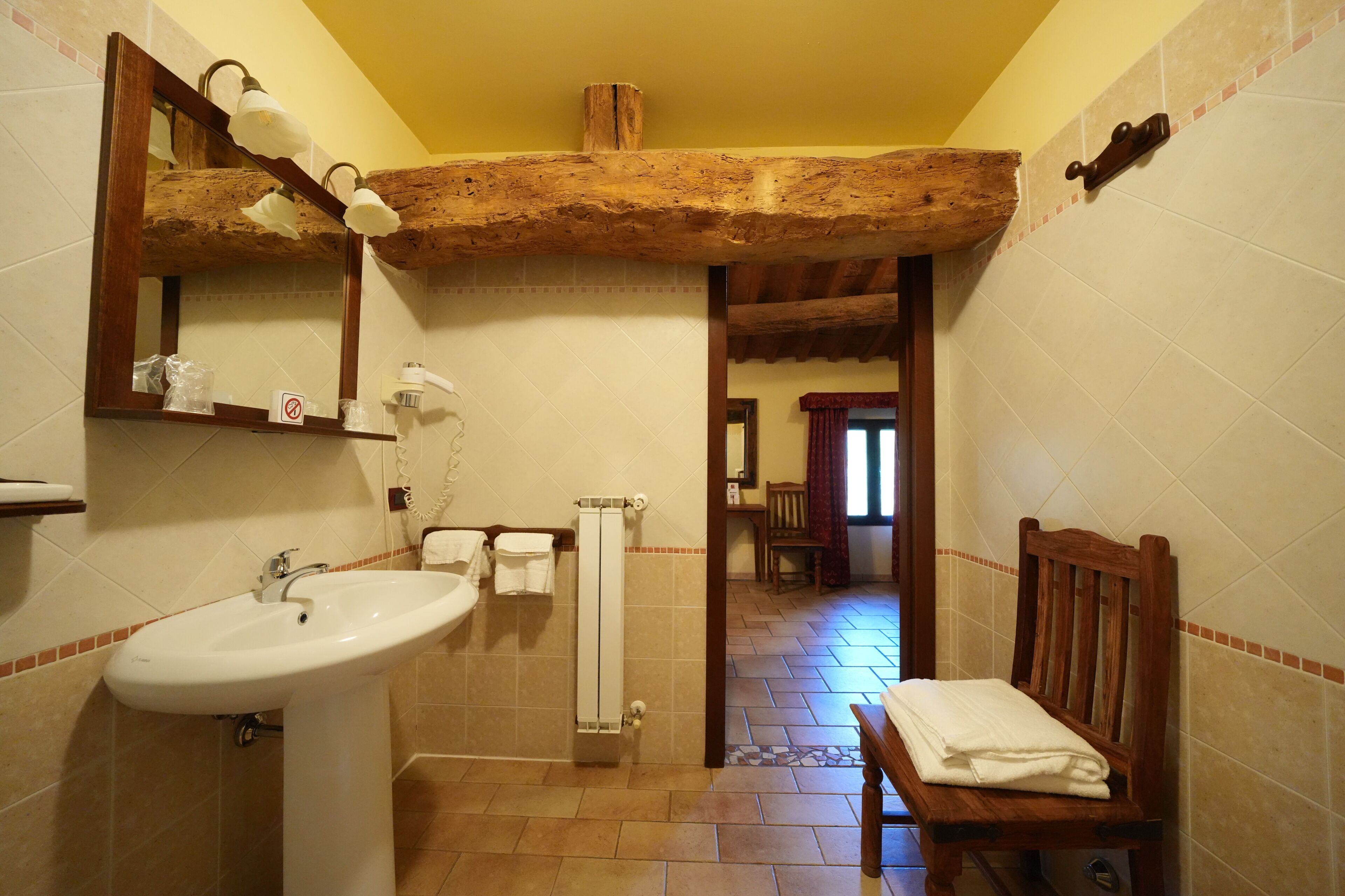Une salle de bain équipée d’un lavabo, d’un miroir, d’un porte-serviettes et d’une chaise en bois.