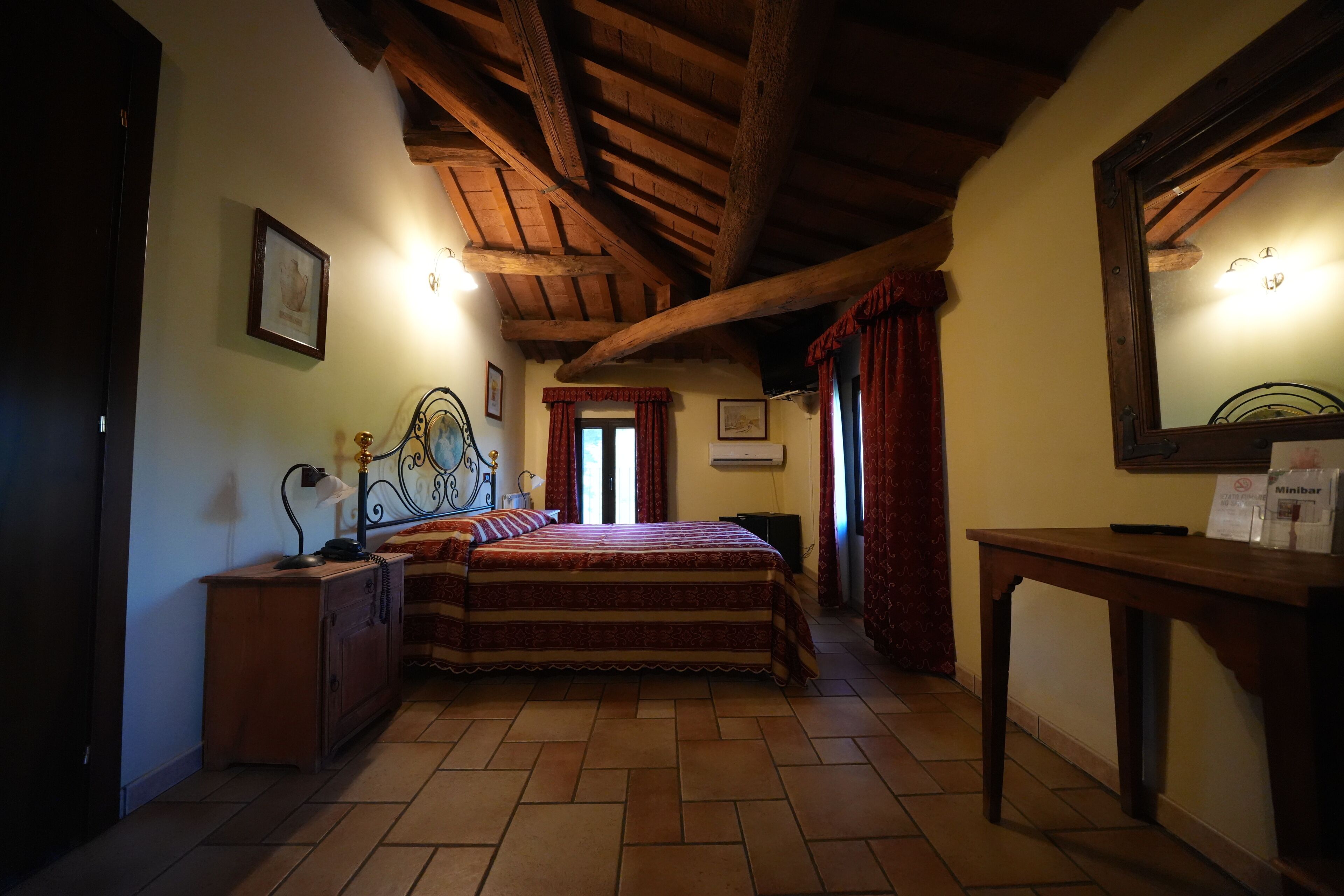 A bedroom with a wooden ceiling, a bed with a patterned bedspread, a bedside table with a lamp, and a nightstand.