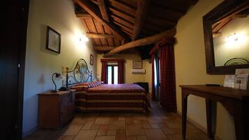 A bedroom with a wooden ceiling, a bed with a patterned bedspread, a bedside table with a lamp, and a nightstand.