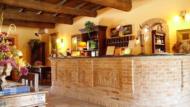 Un área de recepción con mostrador de piedra, vigas de madera, chimenea y una zona de bar con botellas.