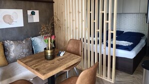 A modern room with a wooden partition, a bed with a patterned headboard, a wooden table with a vase and remote controls, and a sofa with patterned cushions.