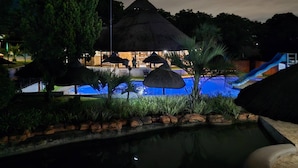 Ein Swimmingpool mit Rutsche, umgeben von tropischer Vegetation und einer strohgedeckten Struktur.