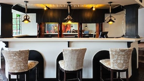 Eine Bar mit einer weißen Theke, drei gepolsterten Barhocker und Pendelleuchten.