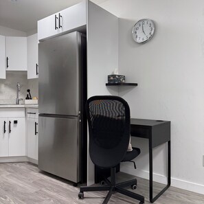 A kitchen with a stainless steel refrigerator, a black office chair, a desk, and a wall clock. - Modern Private Suite in Regina w/ Separate Entrance (Regina)