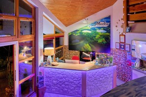 Uma mesa de recepção com um grande cartaz de uma paisagem, teto de madeira e parede de pedra com um relógio.