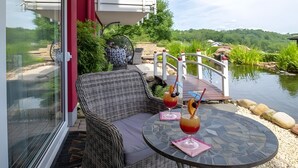 A wicker sofa and a table with drinks on a patio overlooking a pond.