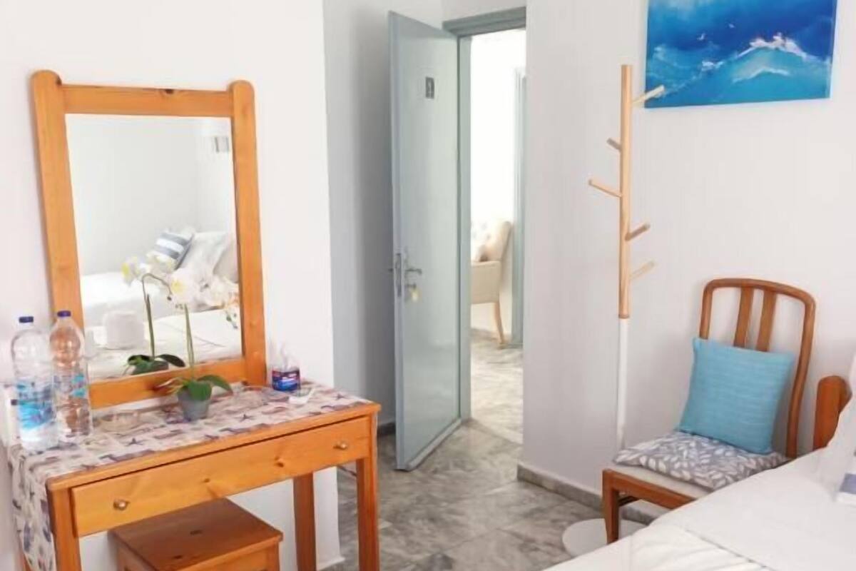 Une pièce comprenant un bureau en bois, une chaise, un lit, un miroir et un tableau accroché au mur.