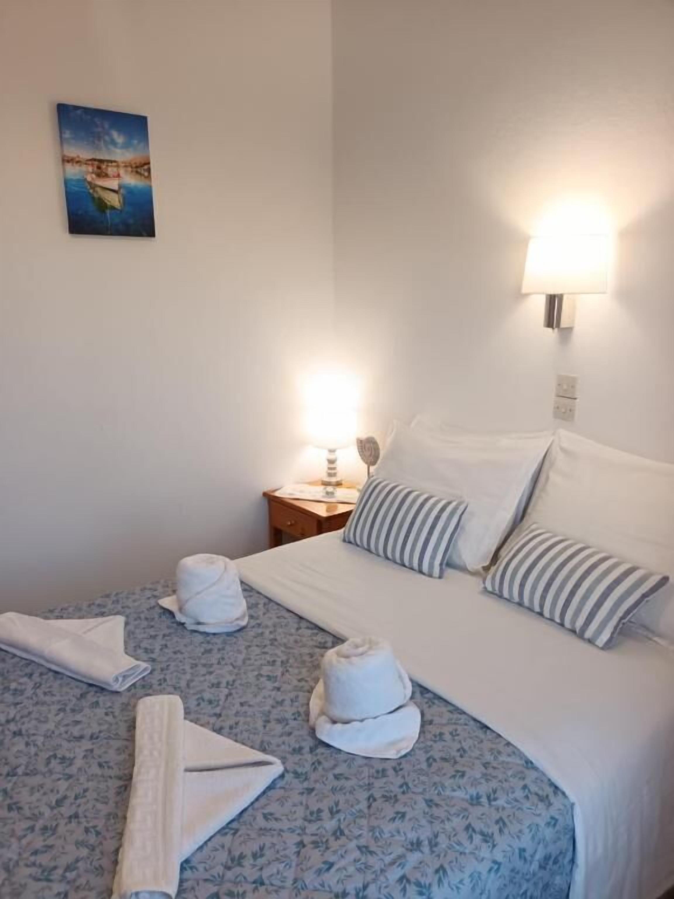 Una habitación de hotel con cama, almohadas, mesita de noche con lámpara y toallas.