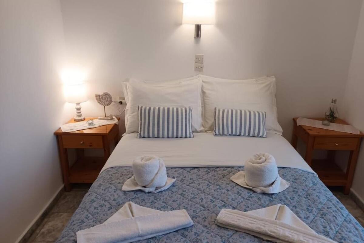 Une chambre d’hôtel avec un lit, deux tables de chevet, une lampe fixée au mur et des serviettes sur le lit.