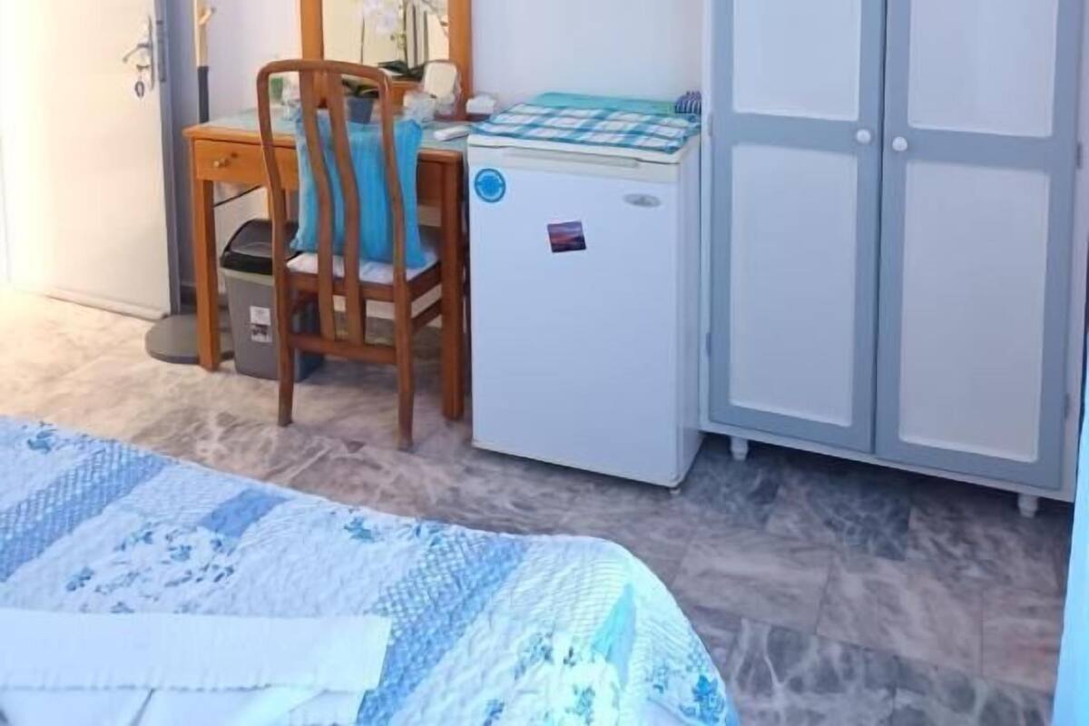 Une chambre à coucher comprenant un lit, un bureau avec une chaise, un petit réfrigérateur, une armoire et un téléviseur posé sur un meuble.