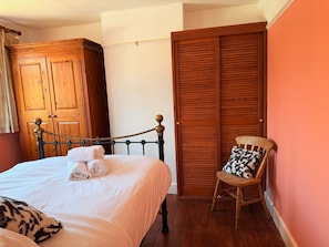 A neatly made bed with a metal headboard, a wooden wardrobe, a wooden chair with a patterned cushion, and a wooden floor. - The Boat Hole - Riverside Living in Cambridge (Cambridge)